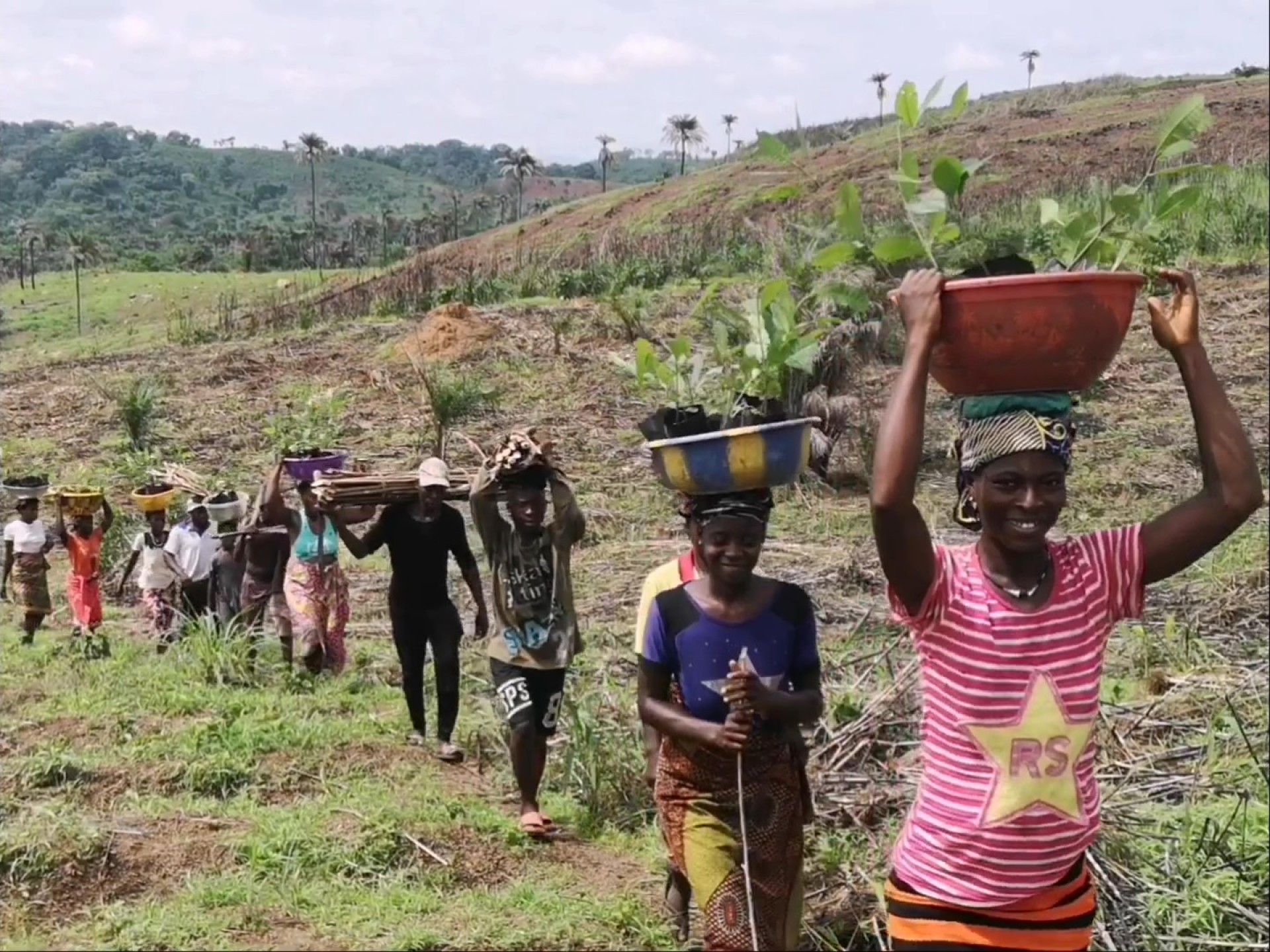 Afrikanische Frauen gehen in einer Reihe hintereinander und tragen Körbe auf dem Kopf