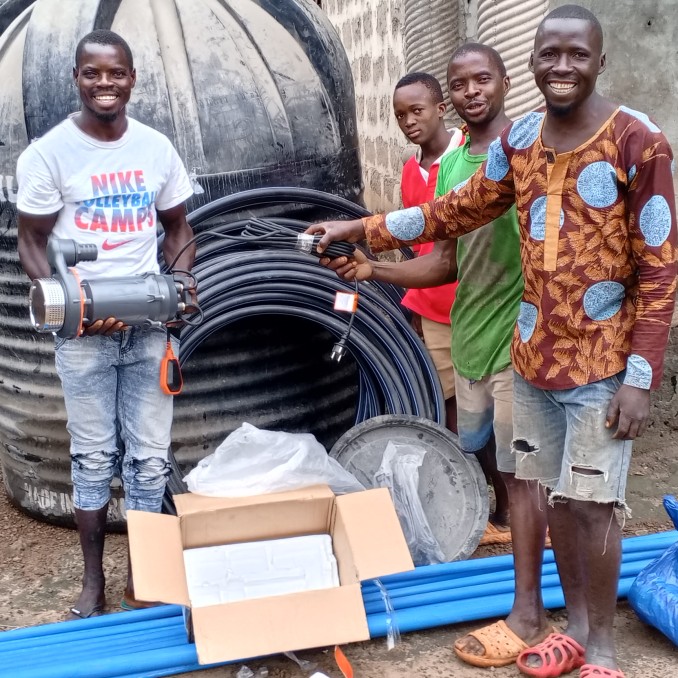 Männer im Impact Village stehen neben Rohren zur Wasserversorgung und Bewässerung