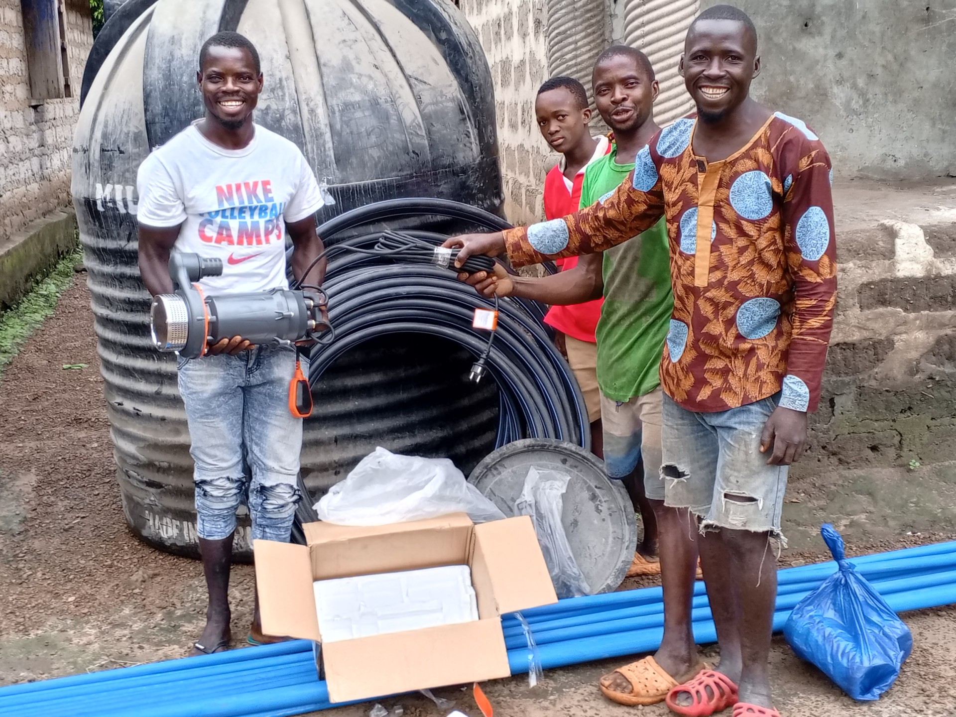 Männer im Impact Village stehen neben Rohren zur Wasserversorgung und Bewässerung
