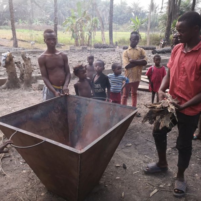 Männer stehen in einem afrikanischen Dort um einen Behälter zum Herstellen von Dünger