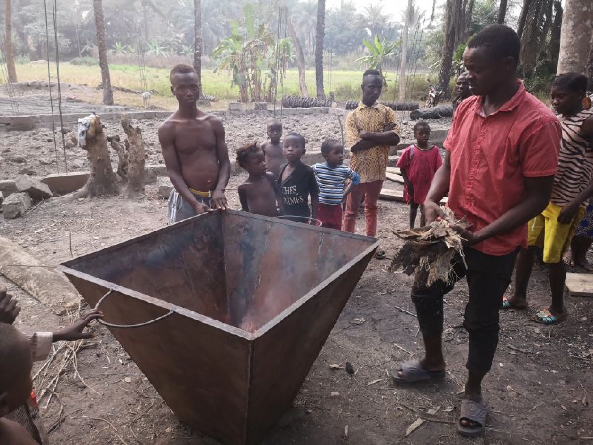 Männer stehen in einem afrikanischen Dort um einen Behälter zum Herstellen von Dünger