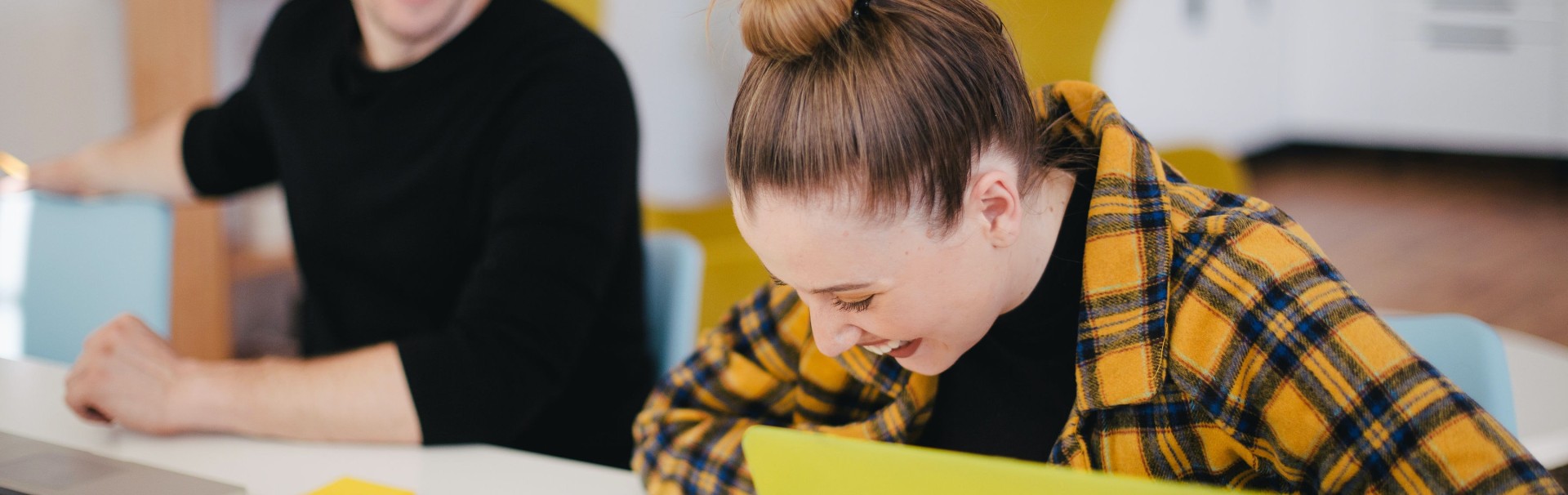 Zwei Kollegen sitzen am Schreibtisch und reden und lachen miteinander
