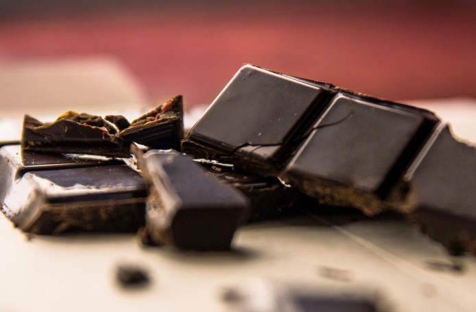 Nahaufnahme von mehreren Stücken dunkler Schokolade und Schokosplitter, die teilweise übereinander liegen.