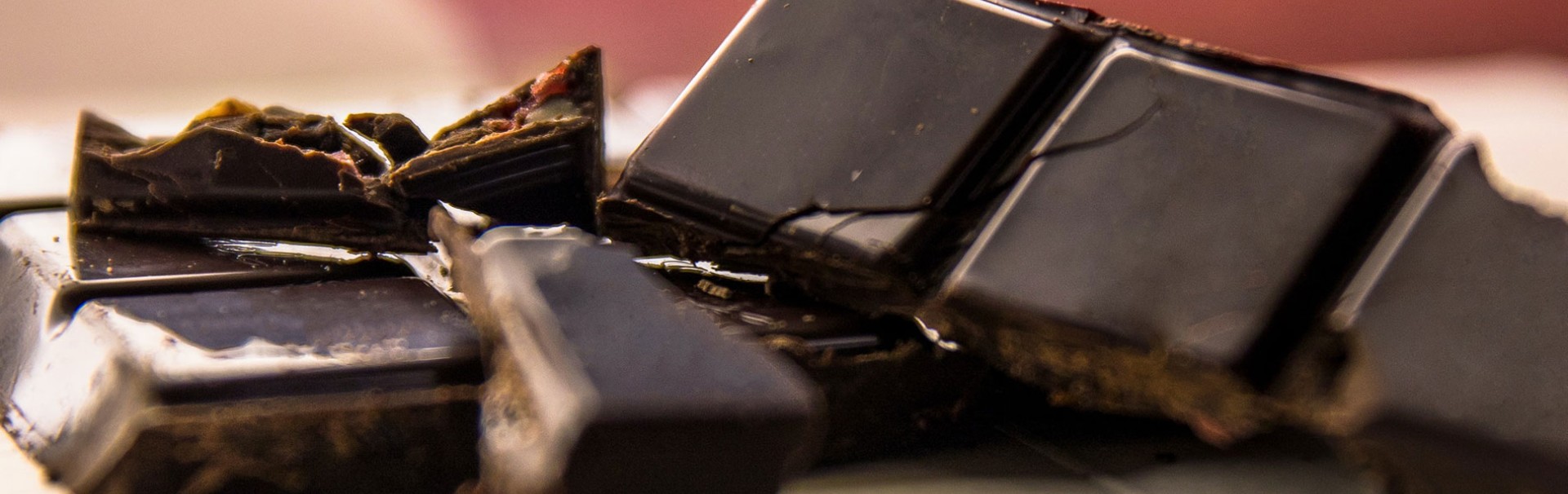 Nahaufnahme von mehreren Stücken dunkler Schokolade und Schokosplitter, die teilweise übereinander liegen.