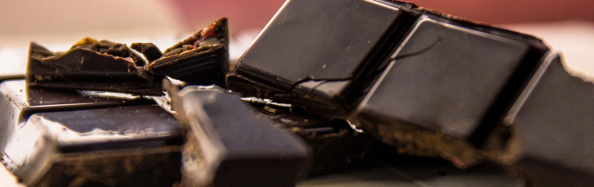 Nahaufnahme von mehreren Stücken dunkler Schokolade und Schokosplitter, die teilweise übereinander liegen.