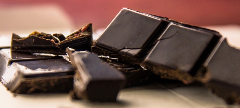 Nahaufnahme von mehreren Stücken dunkler Schokolade und Schokosplitter, die teilweise übereinander liegen.