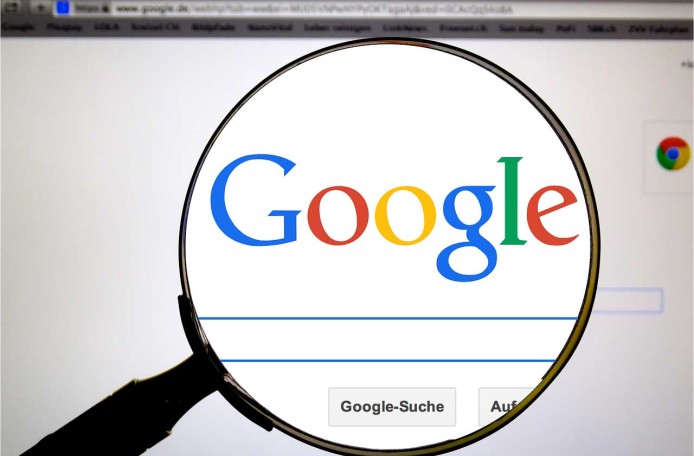 Durch eine Lupe wird der Schriftzug von Google und das Eingabefeld der Suchmaschine vergrößert sichtbar.