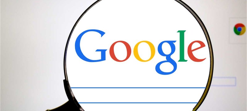 Durch eine Lupe wird der Schriftzug von Google und das Eingabefeld der Suchmaschine vergrößert sichtbar.