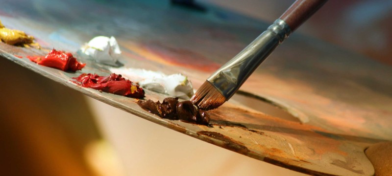 Auf einer Malerpalette sind mehrere Kleckse mit Farbe, und ein Pinsel wird in einen Farbklecks getunkt.