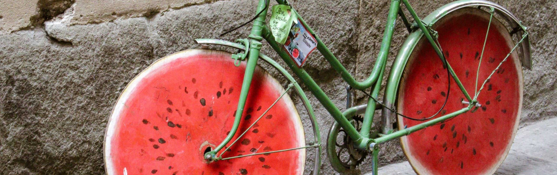 Ein grünes Fahrrad lehnt an einer Wand. Die Räder sehen aus wie eine angeschnittene Wassermelone.