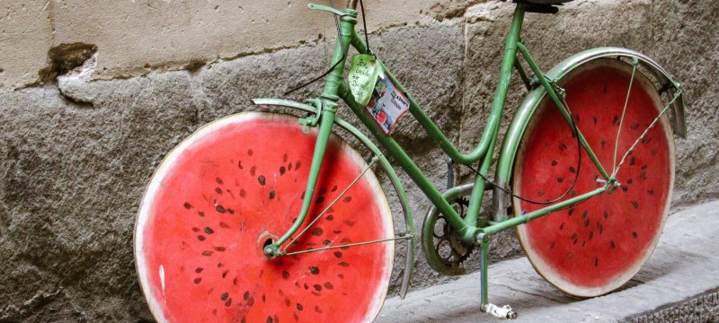 Ein grünes Fahrrad lehnt an einer Wand. Die Räder sehen aus wie eine angeschnittene Wassermelone.