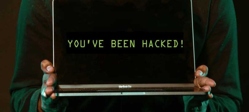 zwei Hände halten einen aufgeklappten Laptop, auf dem Bildschirm steht: You've been hacked.