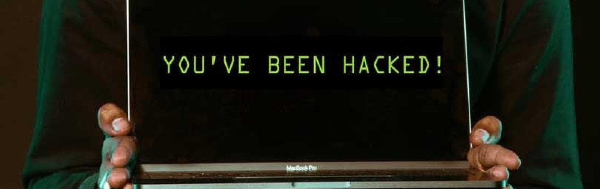 zwei Hände halten einen aufgeklappten Laptop, auf dem Bildschirm steht: You've been hacked.