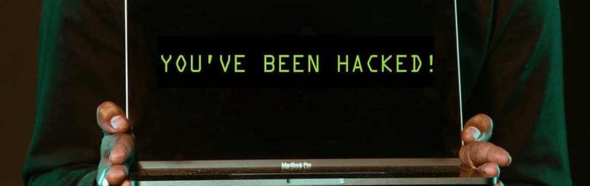 zwei Hände halten einen aufgeklappten Laptop, auf dem Bildschirm steht: You've been hacked.