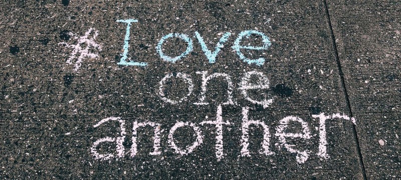 #Love one another steht mit bunter Kreide auf graue Gehwegplatten geschrieben - SCHOKOLADENSEITE.net übernimmt Verantwortung.